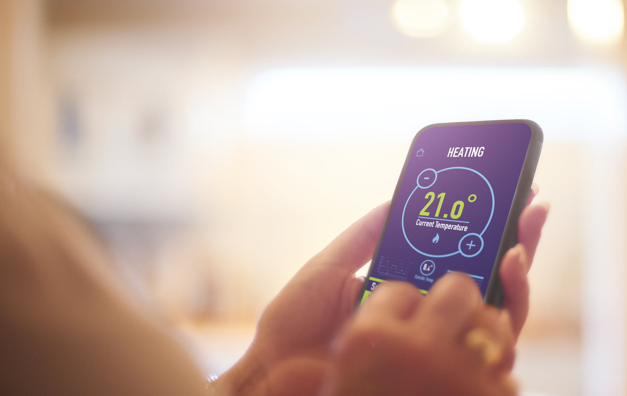 Someone using a thermostat via an app on their smart phone.