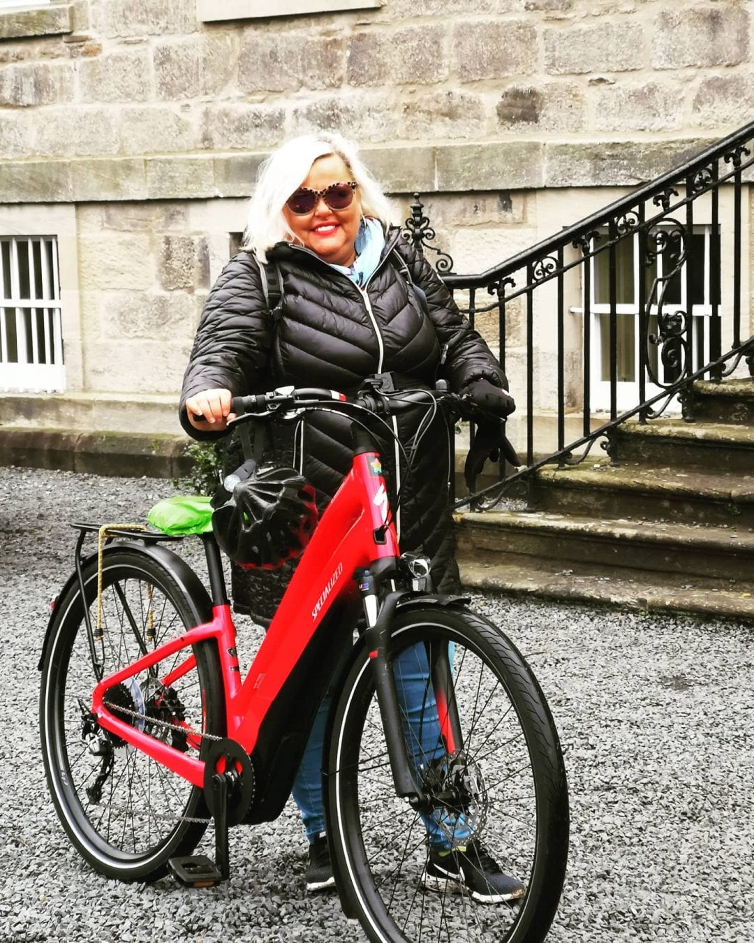 LIsa stands next to her bike with a building in the background.